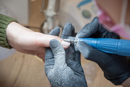 The manicurist grinds off the old coating from the client's nails with the help of a professional electric nail file. High quality photo