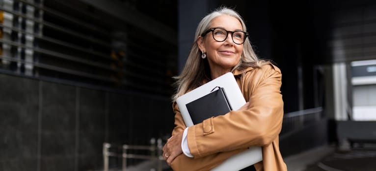 portrait of an elderly businesswoman with a laptop in glasses outside the office.