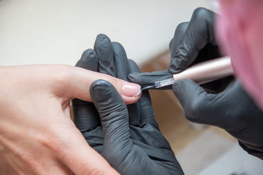 a master does a manicure to a client in a beauty salon and covers her nails with pink varnish. High quality photo