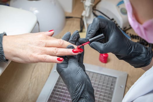 A master manicurist covers the renewed nails of the client with red varnish, Manicure process in beauty salon, High quality photo