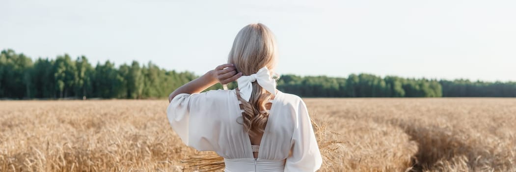 A blonde woman in a long white dress walks in a wheat field. The concept of a wedding and walking in nature.