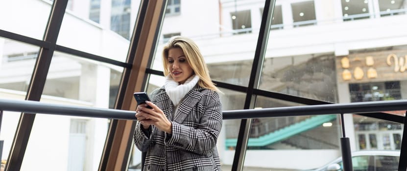 Business woman on the background of a glass facade with a phone in her hands.