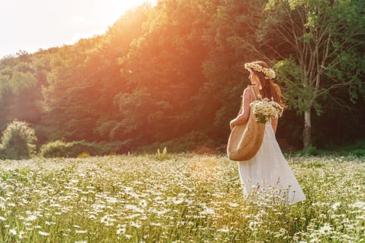 A young woman in a white sundress, a wreath of daisies with a large wicker bag on her shoulder is walking through a field of daisies, against the background of the forest, the sunset light.