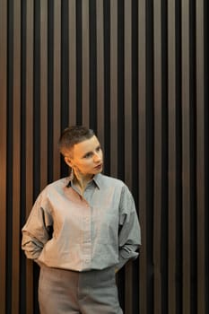 stylish portrait of a woman with a short haircut in a gray shirt against the background of wooden planks.