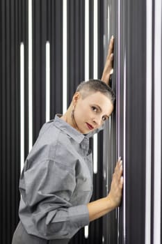 a stylish woman with a short haircut stands leaning against the wall and looks into the camera.