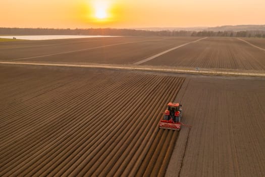 PRAGUE , CZECH REPUBLIC - MARCH 18 2022: Agricultural vehicle leaves long furrows using plow at sunset in rural field. Heavy tractor works in summer evening in countryside aerial view