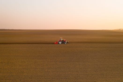 Tractor pulls subsoiler to prepare beds for sowing grain in cultivated field at sunset. Agricultural machinery operates in countryside