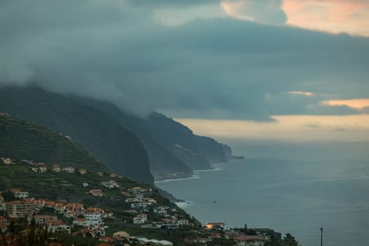 An awe-inspiring landscape of a coastal city, with its majestic mountains reaching out to the sea and surrounded by fog filled clouds. Madeira, Spain