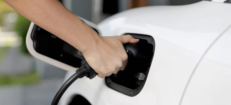 Progressive concept of hand insert an emission-free power connector to the battery of electric vehicle at home. Electric vehicle charging via cable from charging station to EV car battery