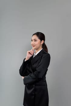 Confident young businesswoman stands on isolated background, posing in formal black suit. Office lady or manager with smart and professional appearance. Enthusiastic