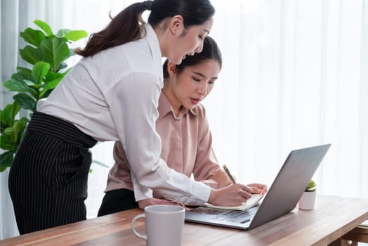 Two young office lady colleagues collaborating in modern office workspace, engaging in discussion and working together on laptop, showcasing their professionalism as modern office worker. Enthusiastic