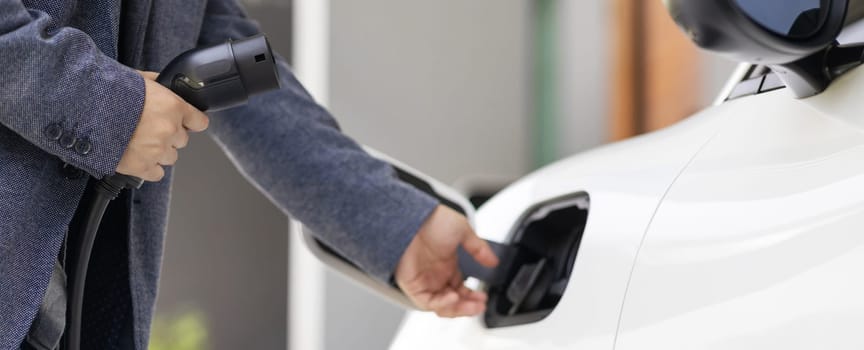 Closeup progressive asian man install cable plug to his electric car with home charging station. Concept of the use of electric vehicles in a progressive lifestyle contributes to clean environment.