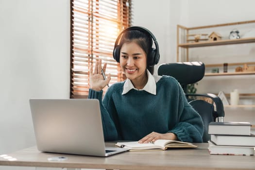 Young asian female wearing with headphones making Video Call on laptop computer. Online education concept.