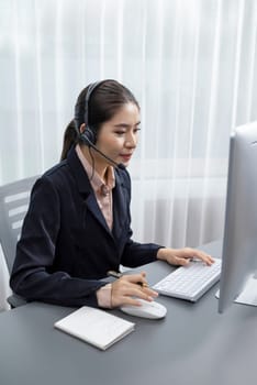 Asian call center with headset and microphone working on her laptop. Female operator provide exceptional customer service. Supportive call center agent helping customer on inquiry. Enthusiastic