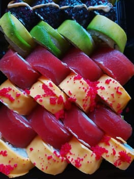 Sushi rolls in a black food box close up top view.