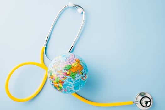 World Health Day. Yellow doctor stethoscope and world globe isolated on pastel blue background with copy space for text, Save world day, Green Earth Environment, Healthcare and medical concept