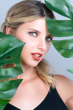 Closeup woman with perfect clean skin and alluring flawless natural soft facial makeup holding green leave monstera. Natural skincare treatment beauty or spa concept in isolated background.