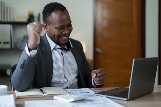 middle aged man American African business man holding computer laptop with hands up in winner is gesture, Happy to be successful celebrating achievement success.