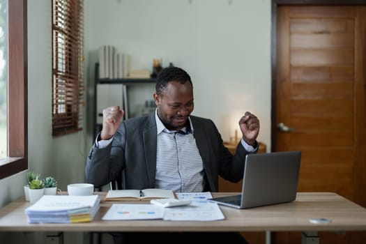middle aged man American African business man holding computer laptop with hands up in winner is gesture, Happy to be successful celebrating achievement success.