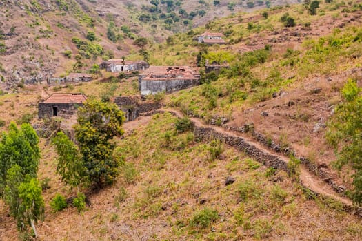 Stone houses and a footpath on a mountain with bushes and grass in the mountainous north of Santiago Island, Cabo Verde