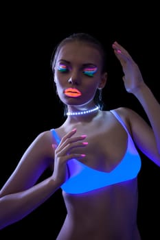 Pretty slim girl dancing under fluorescent light, isolated on black