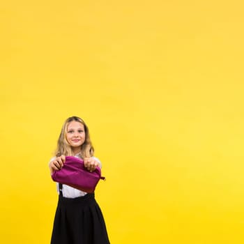 Little teenager girl with pencil case on a yellow background