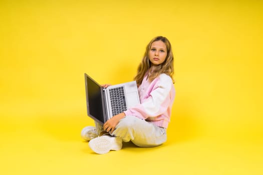 Positive kid sit with a laptop read homework wear casual style cloth isolated over yellow background