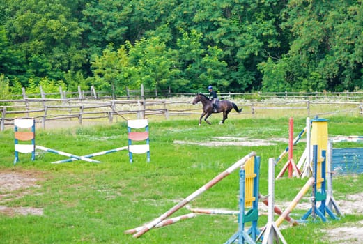 Young rider on horse jumping over obstacle on her course in competition