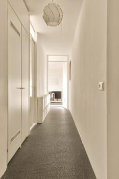 a long hallway with white walls and black carpet on the floor, there is an open door leading to another room