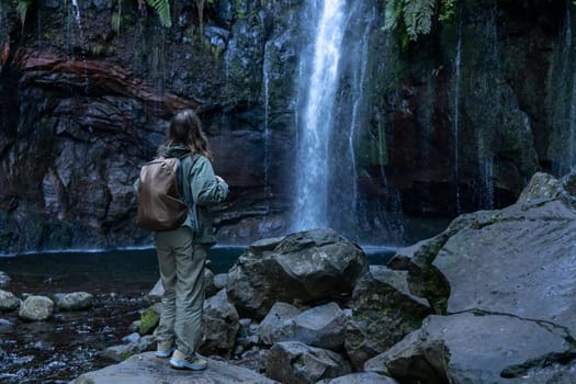 A young girl stands in awe of the majestic beauty of nature, surrounded by a lush landscape with rock and water cascading down a waterfall.