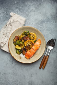 Delicious salmon fillet with grilled Brussels sprouts on plate, rustic stone background top view. Healthy dinner with grilled fish and vegetables, balanced nutrition