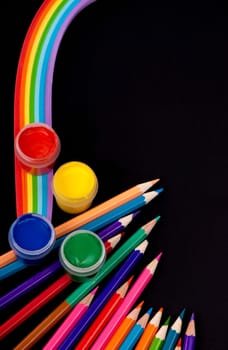 Top view of a blank notebook, a sheet of colored paper, quilling paper, drawing supplies, brushes and colored pencils on a black background. The process of creation, creativity.