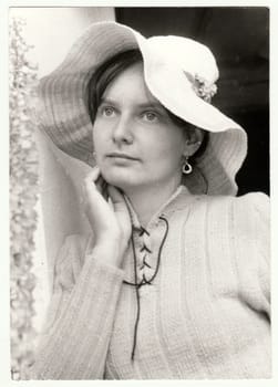 THE CZECHOSLOVAK SOCIALIST REPUBLIC - SEPTEMBER 1982: Vintage photo shows a teenager girl poses outdoors. She wears a romantic woman hat. Retro black and white photography. Circa 1980.