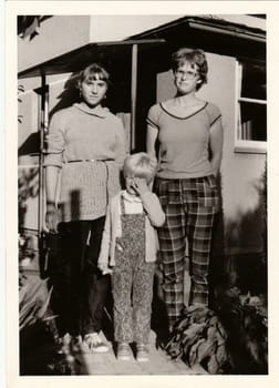 THE CZECHOSLOVAK SOCIALIST REPUBLIC - CIRCA 1980s: Vintage photo shows young girls and child in front of country house. Retro black and white photography. Circa 1980.