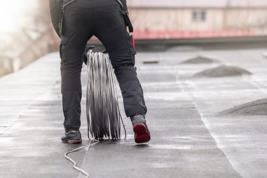 Ground wire. A worker lays a ground cable on the roof of a building. Electrician fixing aluminum wire for grounding solar panels.