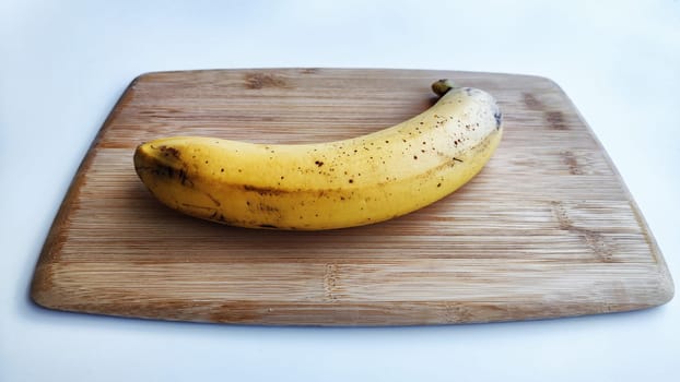 Banana with peel on wooden board and white background. Ripe banana with peel, Close up. Delicious sweet fruit dessert