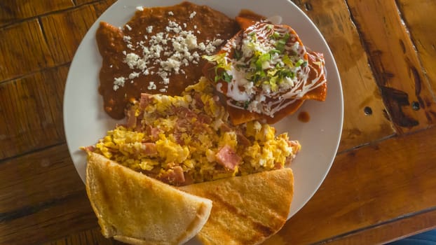 Chilaquiles and refried beans, traditional Mexican breakfast, served with scrambled eggs and ham and toasted bread. Baja California, Mexico.