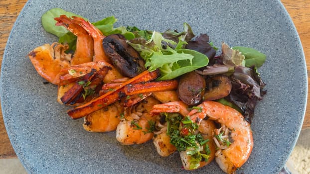 Shrimp with garlic butter and chimichurri sauce, camarones al ajo, delicious Mexican seafood dish with salad leaves on grey stone plate.