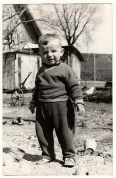 THE CZECHOSLOVAK SOCIALIST REPUBLIC - CIRCA 1970s: Vintage photo shows a small boy stands in the backyard. Retro black and white photography. Circa 1970.