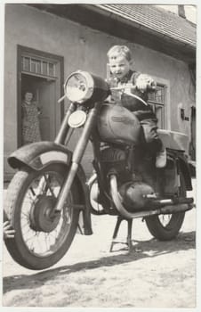 THE CZECHOSLOVAK SOCIALIST REPUBLIC - CIRCA 1960s: Vintage photo shows boy sits on the vintage motorcycle. Retro black and white photography. Circa 1960.