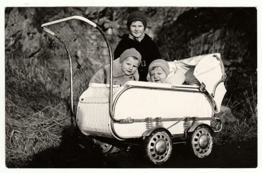 THE CZECHOSLOVAK SOCIALIST REPUBLIC - CIRCA 1950s: Vintage photo shows small children and baby in the pram - carriage in the wintertime. Retro black and white photography. Circa 1950.