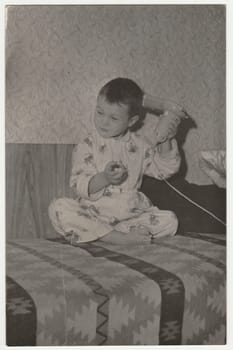 THE CZECHOSLOVAK SOCIALIST REPUBLIC - CIRCA 1970s: Vintage photo shows a small boy wears pyjamas and he uses hair dryer. Funny photography of a cute boy. Retro black and white photography. Circa 1970.
