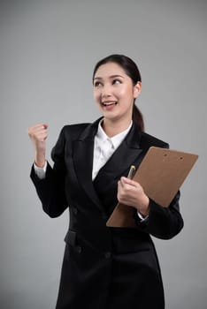 Confident young asian businesswoman in formal suit holding clipboard with hand gesture indicating promotion or advertising with surprised facial expression on isolated background. Enthusiastic