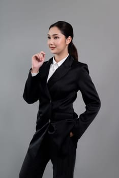 Confident young businesswoman stands on isolated background, posing in formal black suit. Office lady or manager with smart and professional appearance. Enthusiastic