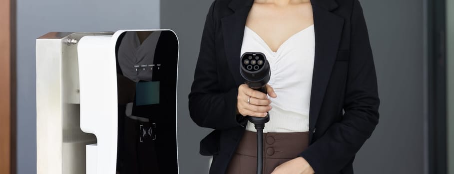 Closeup asian woman holding and pointing an EV plug, a home charging station providing a sustainable power source for electric vehicles. Alternative energy for progressive lifestyle.