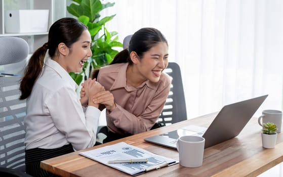 Two young office lady colleagues collaborating in modern office workspace, engaging in discussion and working together on laptop, showcasing their professionalism as modern office worker. Enthusiastic