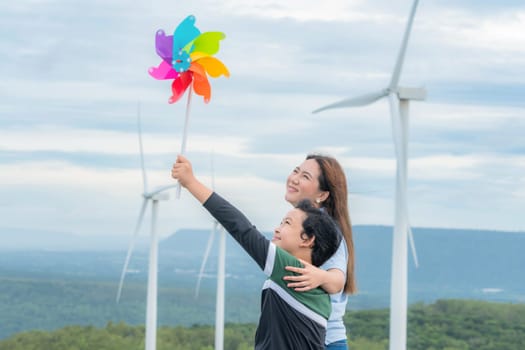 A progressive mother and her son are on vacation, enjoying the natural beauty of a lake at the bottom of a hill while the boy carries a toy windmill.