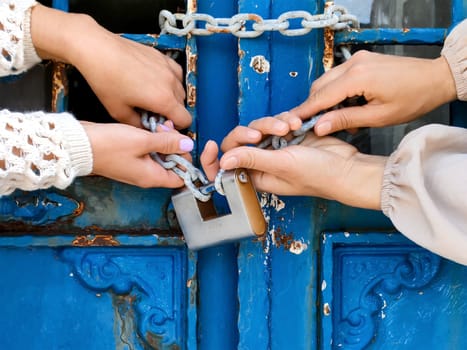 Women's hands are trying to break thick chain with padlock to open old door, close-up