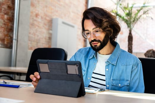 Young caucasian man with eyeglasses working with digital tablet in coworking space. Copy space. Startup concept.