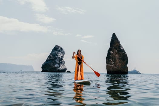 Close up shot of beautiful young caucasian woman with black hair and freckles looking at camera and smiling. Cute woman portrait in a pink bikini posing on a volcanic rock high above the sea